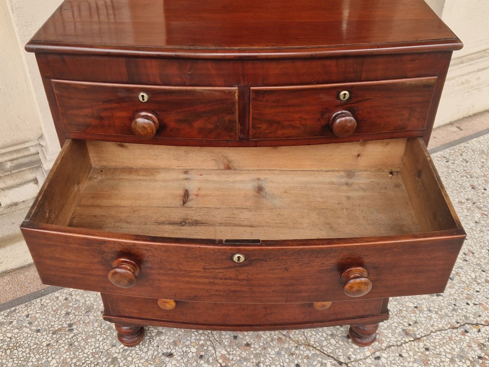 A Victorian mahogany bow fronted chest of drawers featuring two short over three long drawers with turned wooden handles and brass escutcheons on turned feet. View V