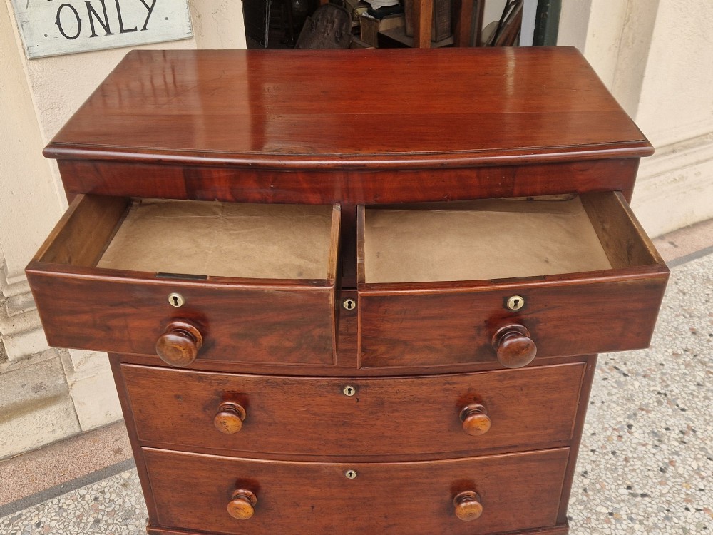 A Victorian mahogany bow fronted chest of drawers featuring two short over three long drawers with turned wooden handles and brass escutcheons on turned feet. View VI