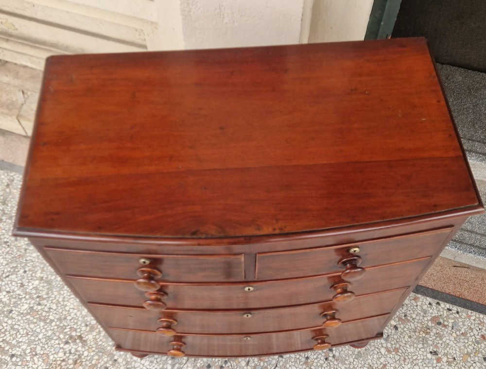 A Victorian mahogany bow fronted chest of drawers featuring two short over three long drawers with turned wooden handles and brass escutcheons on turned feet. View VIII