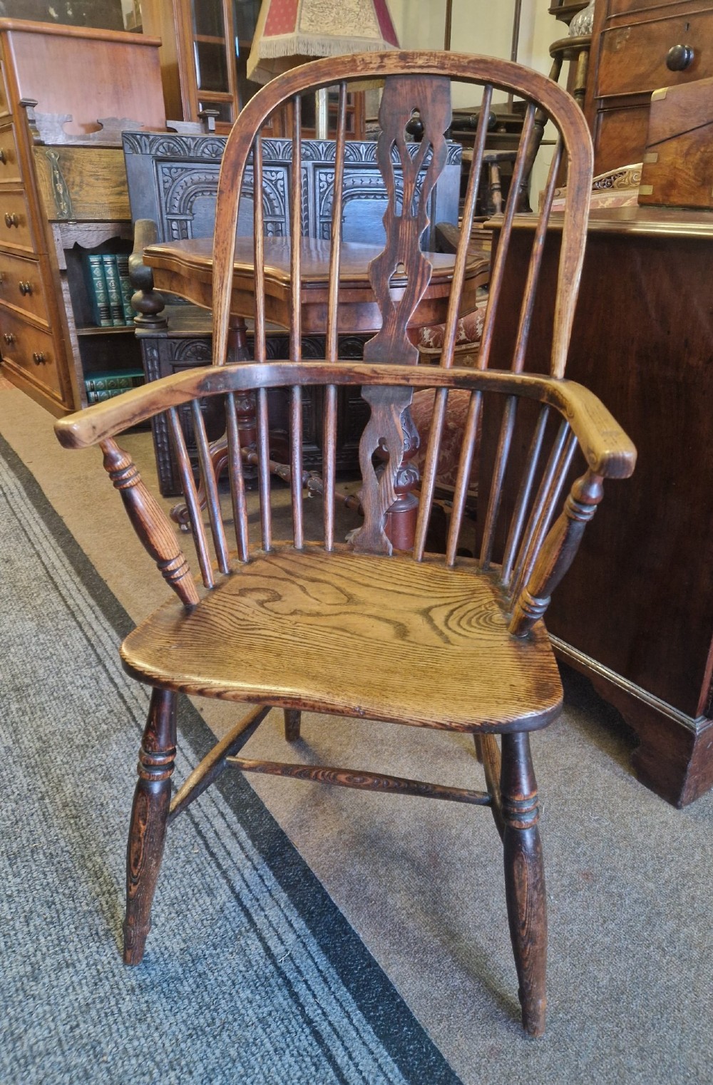 An antique ash and elm Windsor armchair with a hoop back, central pierced splat, turned spindles, shaped wooden seat, and turned legs joined by an H-stretcher.