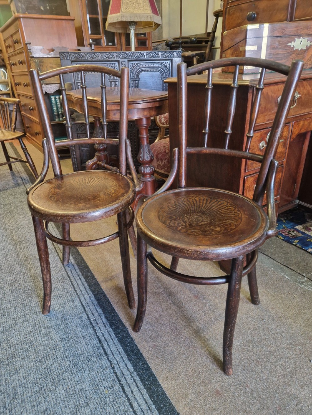 A pair of dark brown bentwood bistro chairs featuring spindle backrests and round wooden seats with embossed decorative shell motifs.