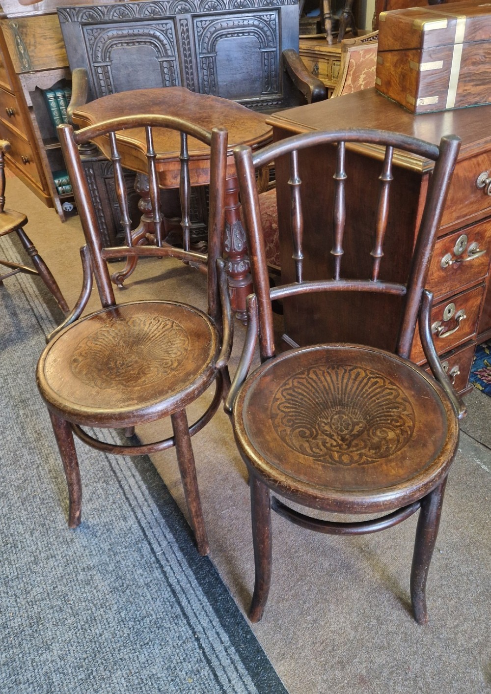A pair of dark brown bentwood bistro chairs featuring spindle backrests and round wooden seats with embossed decorative shell motifs. View II