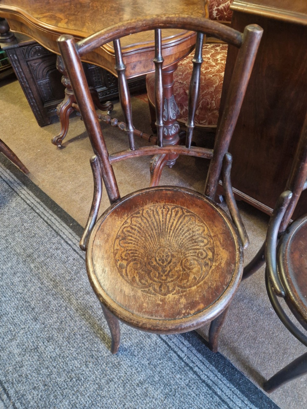 A pair of dark brown bentwood bistro chairs featuring spindle backrests and round wooden seats with embossed decorative shell motifs. View III