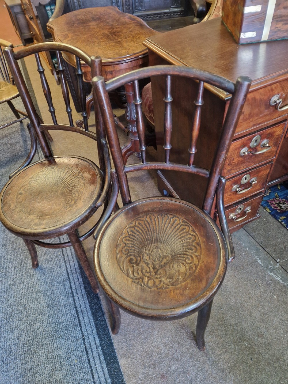 A pair of dark brown bentwood bistro chairs featuring spindle backrests and round wooden seats with embossed decorative shell motifs. View IV