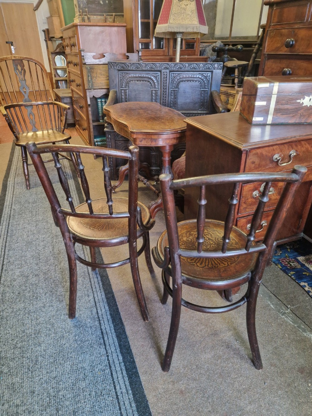A pair of dark brown bentwood bistro chairs featuring spindle backrests and round wooden seats with embossed decorative shell motifs. View V