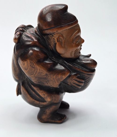 fig 2. A carved dark wood Japanese figurine depicting Ebisu holding a basket containing a sea bream fish.