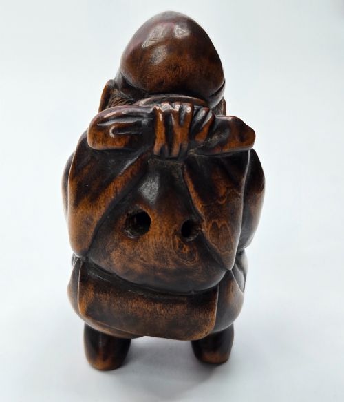 fig 1. A carved dark wood Japanese figurine depicting Ebisu holding a basket containing a sea bream fish.