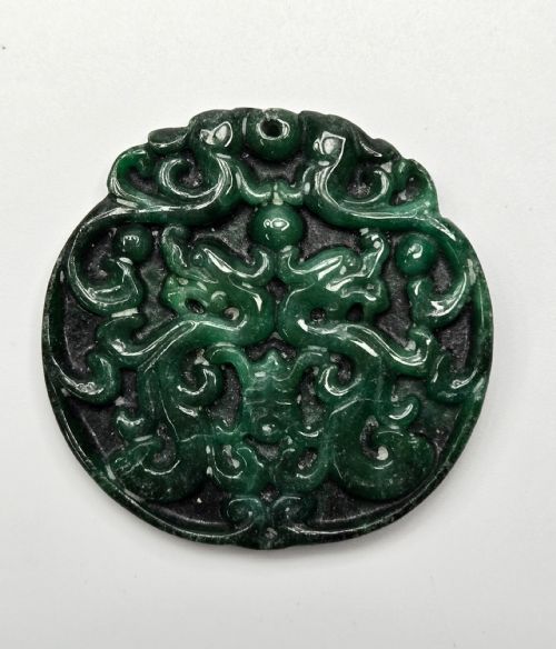 fig 1. A circular dark green carved jadeite pendant featuring stylised double dragon motifs with openwork details and a suspension hole at the top.