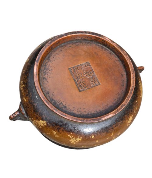fig 3. A dark brown cast bronze incense burner featuring irregular gold splash decoration and detailed beast mask handles on either side.