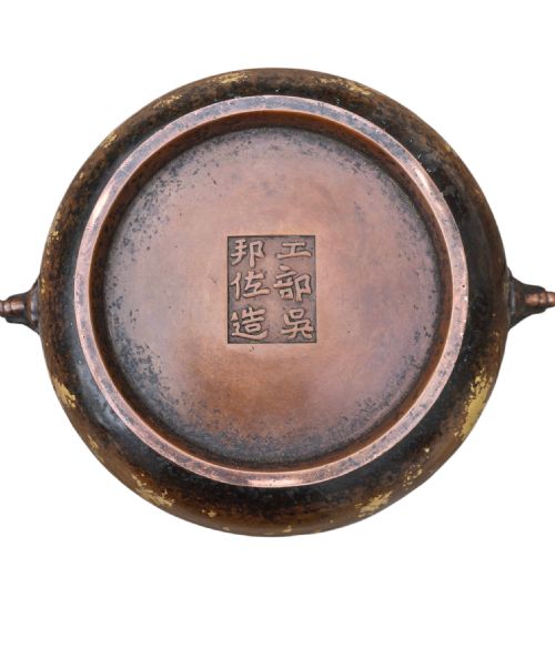 fig 4. A dark brown cast bronze incense burner featuring irregular gold splash decoration and detailed beast mask handles on either side.