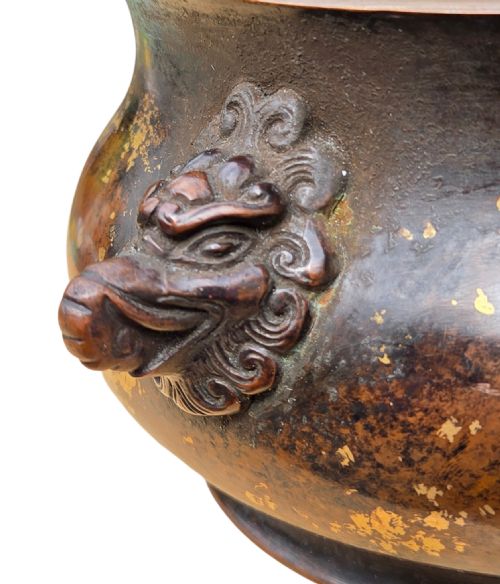 fig 8. A dark brown cast bronze incense burner featuring irregular gold splash decoration and detailed beast mask handles on either side.