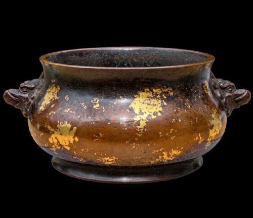 fig 1. A dark brown cast bronze incense burner featuring irregular gold splash decoration and detailed beast mask handles on either side.
