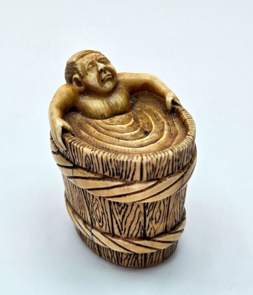 fig 1. A small carved stag antler netsuke depicting a man sitting inside a wooden bath tub with carved water ripples.