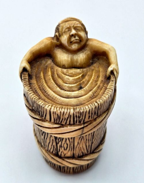 fig 2. A small carved stag antler netsuke depicting a man sitting inside a wooden bath tub with carved water ripples.