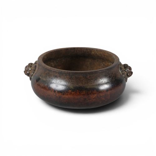 fig 2. A heavy dark brown cast bronze incense burner featuring a low compressed circular form decorated with relief beast mask handles.