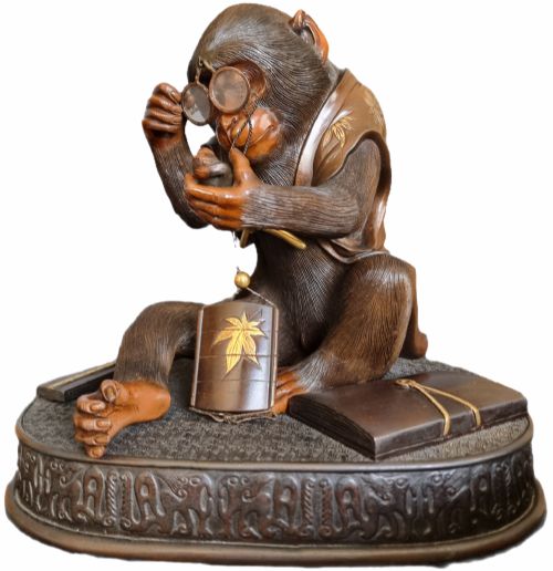 fig 3. A dark bronze Japanese okimono sculpture depicting an anthropomorphic monkey wearing spectacles, seated with a book and inro.