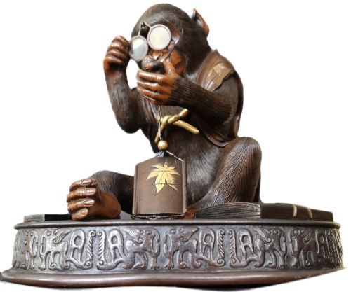 fig 4. A dark bronze Japanese okimono sculpture depicting an anthropomorphic monkey wearing spectacles, seated with a book and inro.