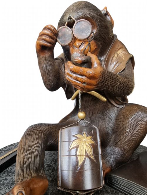 fig 6. A dark bronze Japanese okimono sculpture depicting an anthropomorphic monkey wearing spectacles, seated with a book and inro.