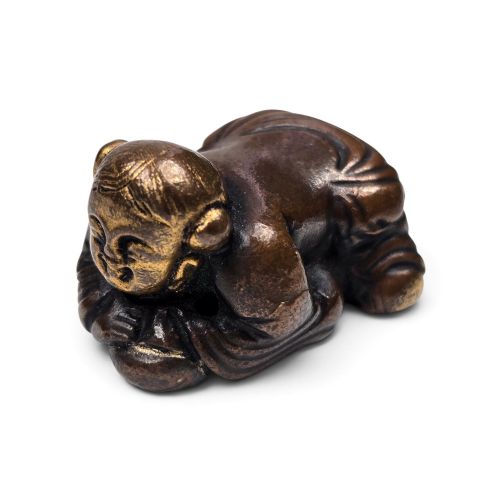 fig 1. A dark bronze cast sculpture of a reclining child with gilded details on the head and face, resting on a flat base.