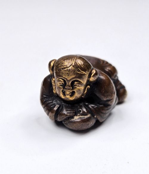 fig 2. A dark bronze cast sculpture of a reclining child with gilded details on the head and face, resting on a flat base.