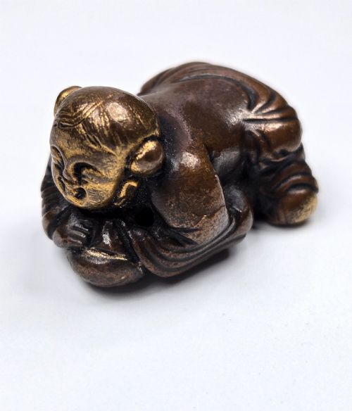 fig 3. A dark bronze cast sculpture of a reclining child with gilded details on the head and face, resting on a flat base.