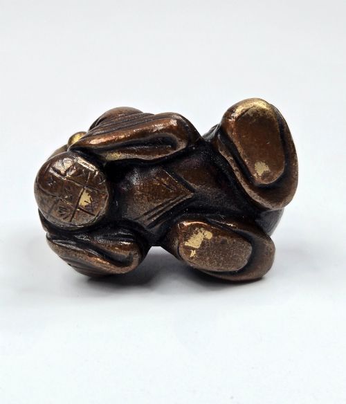 fig 4. A dark bronze cast sculpture of a reclining child with gilded details on the head and face, resting on a flat base.