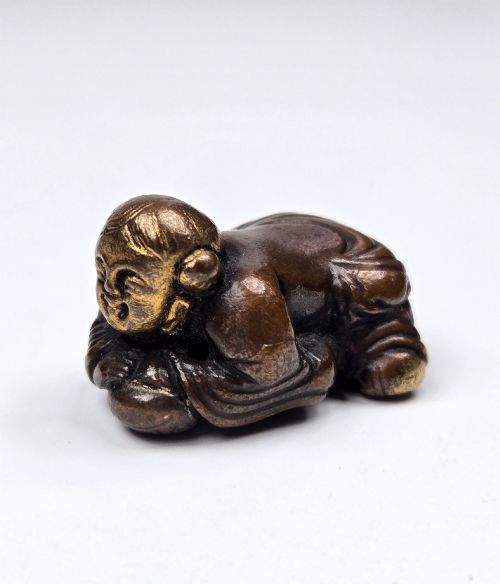 fig 5. A dark bronze cast sculpture of a reclining child with gilded details on the head and face, resting on a flat base.
