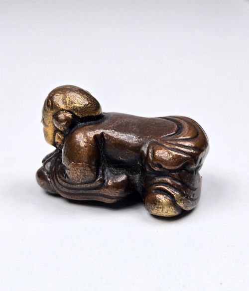 fig 6. A dark bronze cast sculpture of a reclining child with gilded details on the head and face, resting on a flat base.