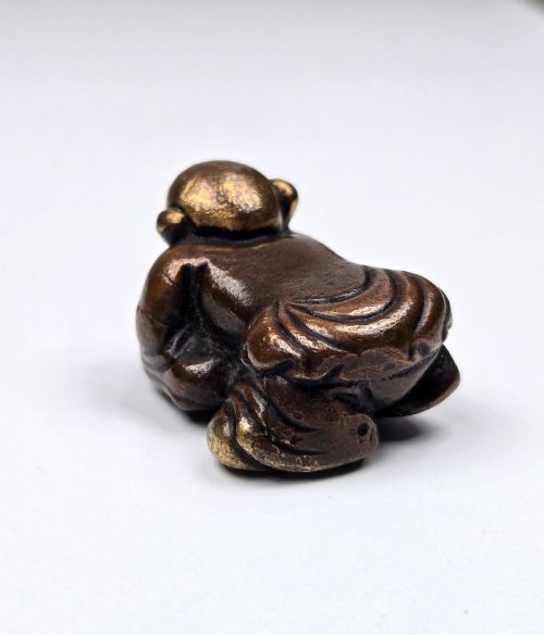 fig 7. A dark bronze cast sculpture of a reclining child with gilded details on the head and face, resting on a flat base.