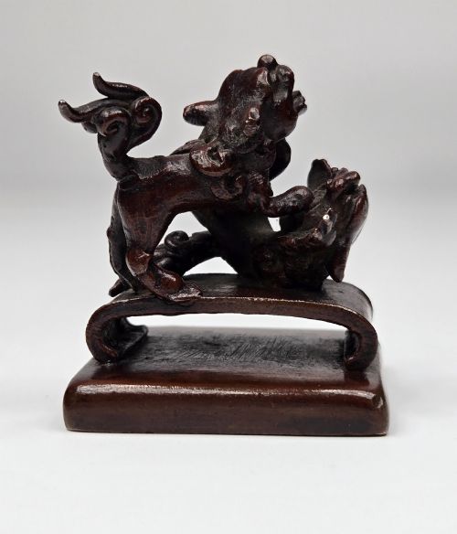 fig 2. A dark bronze Chinese scholars seal topped with two sculptural wrestling shishi lions resting on an arched platform atop a square base.