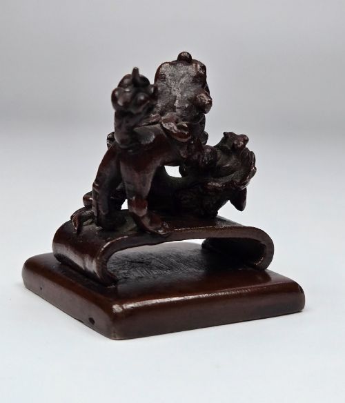 fig 3. A dark bronze Chinese scholars seal topped with two sculptural wrestling shishi lions resting on an arched platform atop a square base.