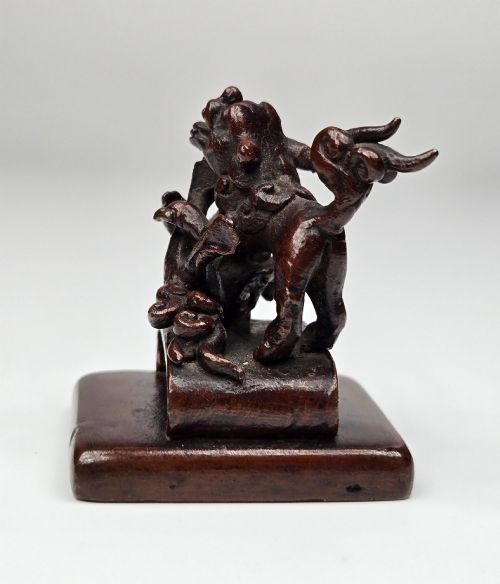 fig 4. A dark bronze Chinese scholars seal topped with two sculptural wrestling shishi lions resting on an arched platform atop a square base.