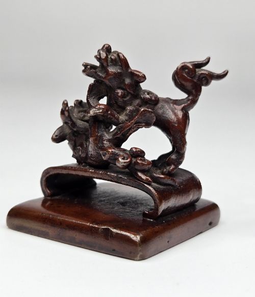 fig 5. A dark bronze Chinese scholars seal topped with two sculptural wrestling shishi lions resting on an arched platform atop a square base.