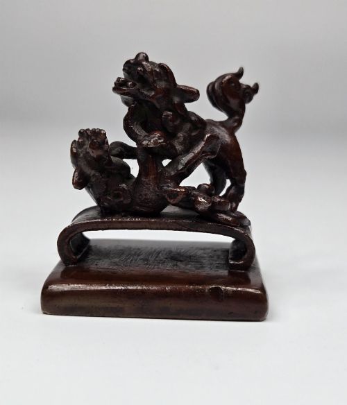 fig 6. A dark bronze Chinese scholars seal topped with two sculptural wrestling shishi lions resting on an arched platform atop a square base.