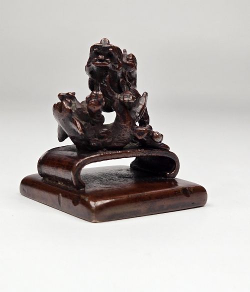 fig 7. A dark bronze Chinese scholars seal topped with two sculptural wrestling shishi lions resting on an arched platform atop a square base.