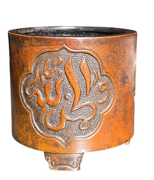 fig 1. A cylindrical warm brown bronze tripod censer featuring a raised lobed cartouche with Arabic calligraphy set against a textured ground.