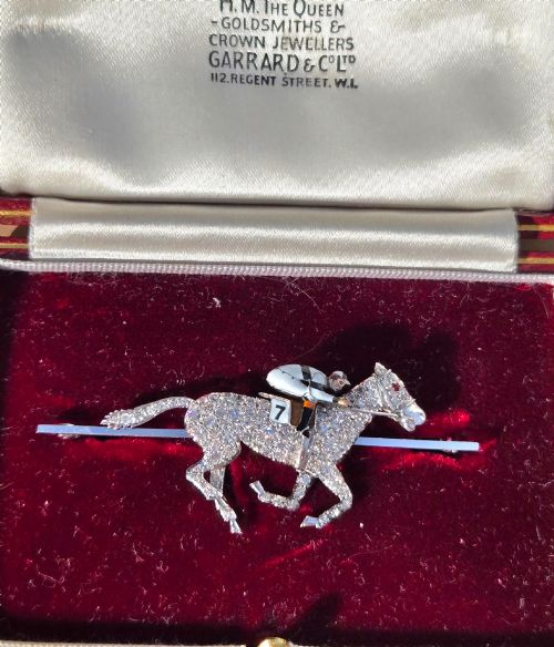 fig 1. A platinum-topped 18ct gold brooch shaped as a galloping racehorse set with diamonds, ridden by a jockey in black and white enamel silks with number seven.