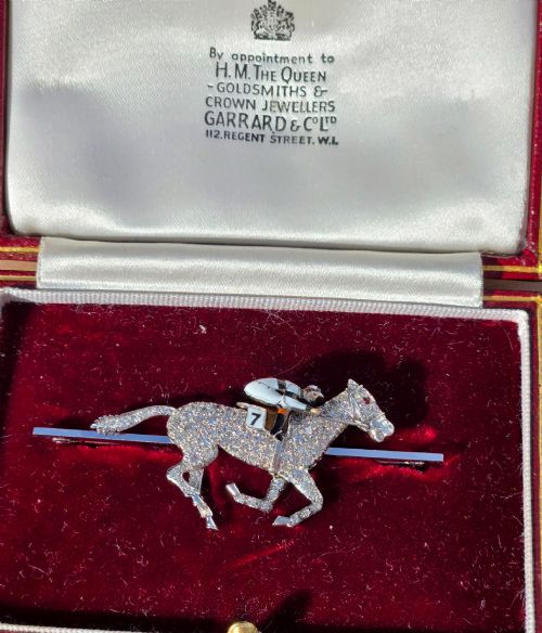 fig 2. A platinum-topped 18ct gold brooch shaped as a galloping racehorse set with diamonds, ridden by a jockey in black and white enamel silks with number seven.