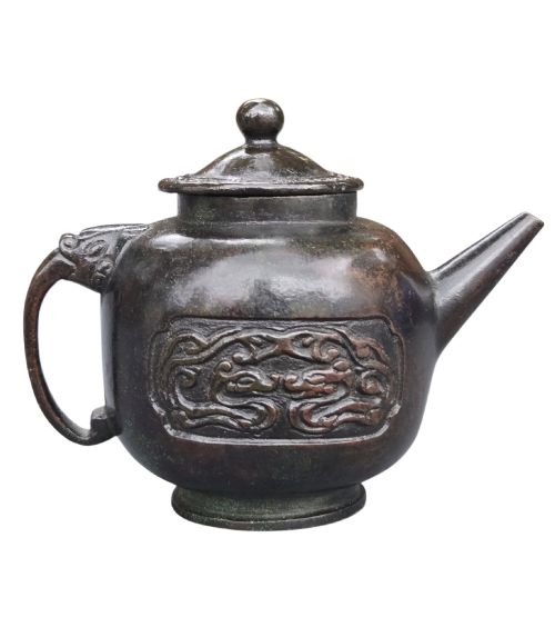 fig 3. A dark patinated cast bronze vessel in ewer form featuring a dragon-head handle, a tapered spout, and carved relief panels.