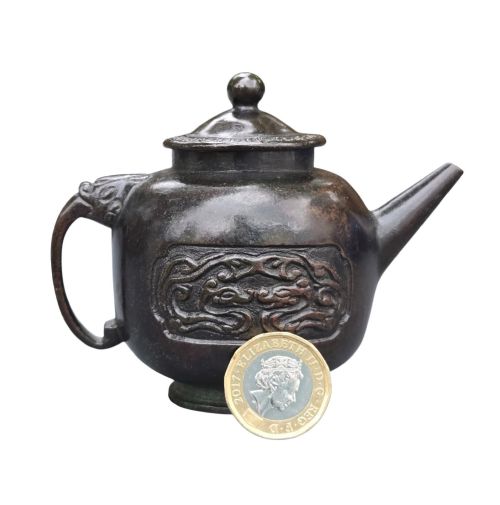 fig 5. A dark patinated cast bronze vessel in ewer form featuring a dragon-head handle, a tapered spout, and carved relief panels.