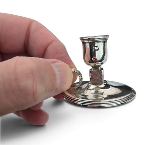 fig 1. A small George III sterling silver taperstick featuring a flared sconce, a square central collar, a side ring handle, and a moulded circular base.