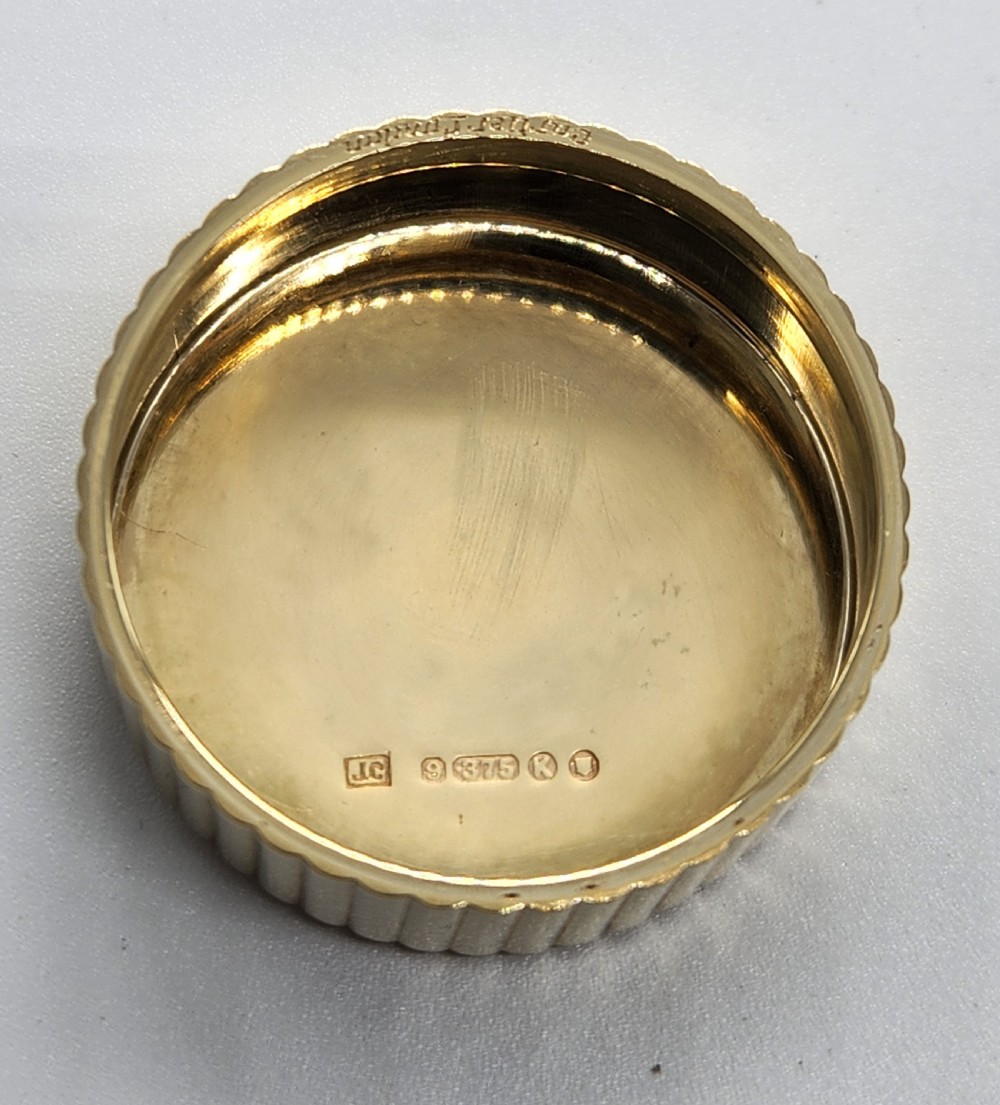 A circular polished yellow gold box featuring vertical fluted sides and a hinged semicircular handle with visible hallmarks. View III
