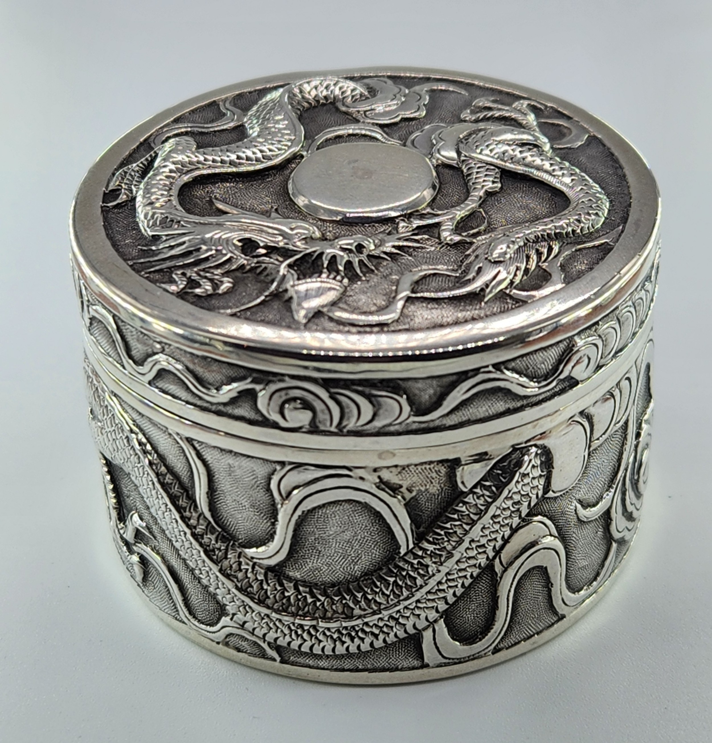 A circular antique Chinese export silver box decorated with high-relief dragon repousse carvings on the lid and side walls.