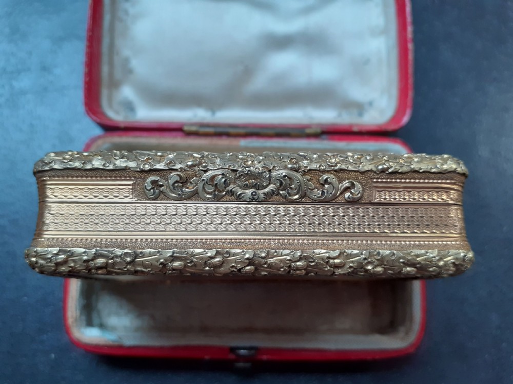 A rectangular 18 carat gold snuff box featuring engine-turned panels surrounded by a chased foliate border. View III