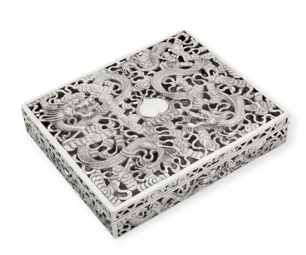 A rectangular silver box featuring detailed pierced openwork of two dragons amidst clouds around a central pearl.