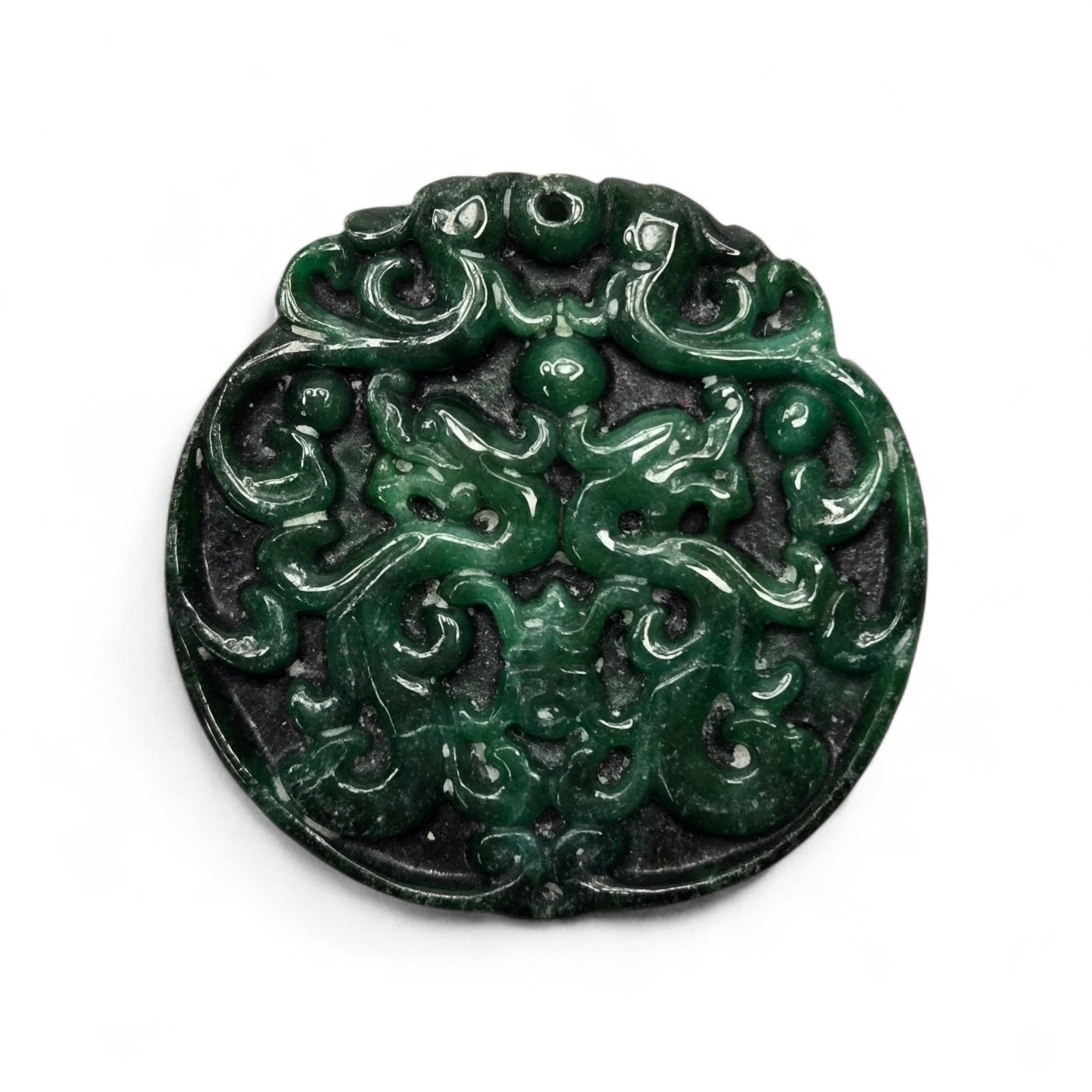 A circular dark green carved jadeite pendant featuring stylised double dragon motifs with openwork details and a suspension hole at the top.