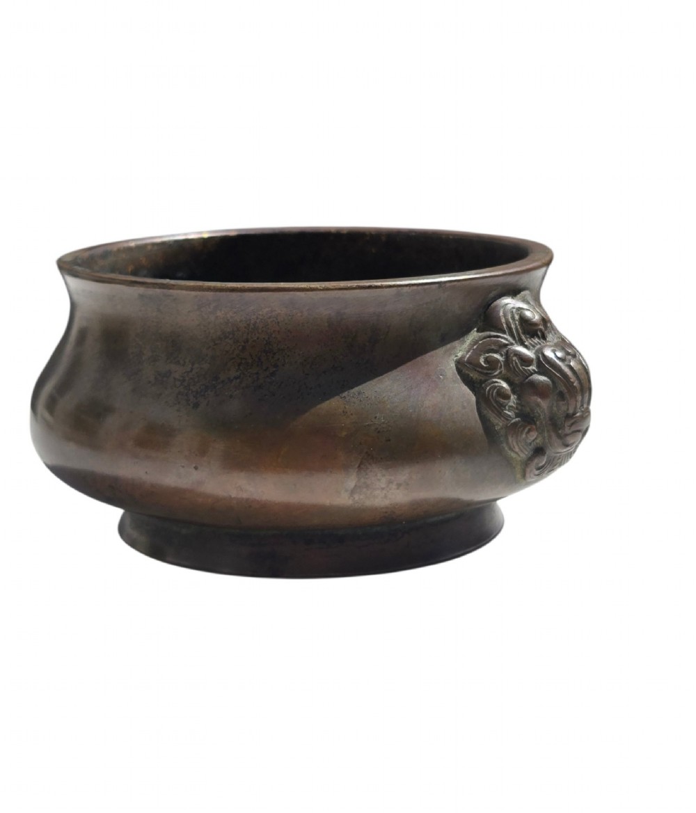 A cast bronze censer featuring a flared rim, compressed globular body, low circular foot, and cast relief taotie mask handles on the side. View II