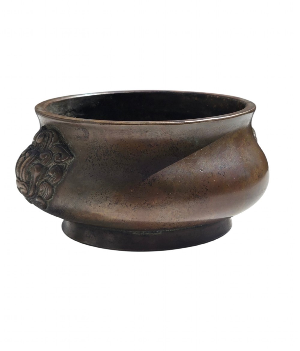 A cast bronze censer featuring a flared rim, compressed globular body, low circular foot, and cast relief taotie mask handles on the side. View IV