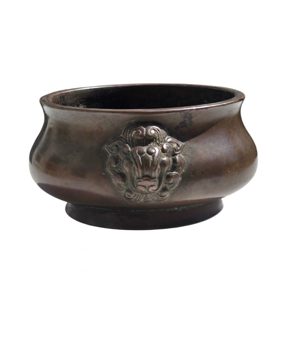 A cast bronze censer featuring a flared rim, compressed globular body, low circular foot, and cast relief taotie mask handles on the side.