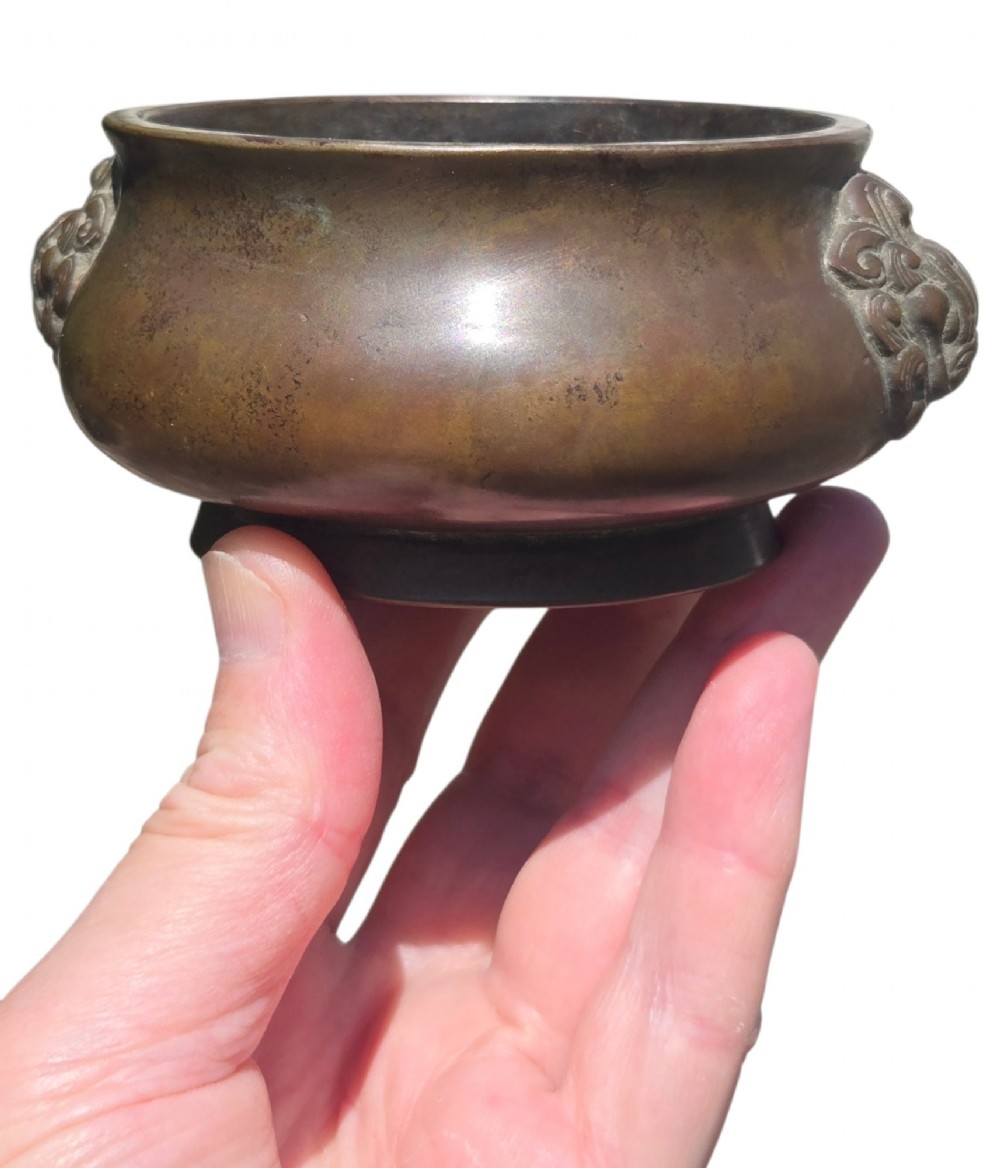A cast bronze censer featuring a flared rim, compressed globular body, low circular foot, and cast relief taotie mask handles on the side. View X